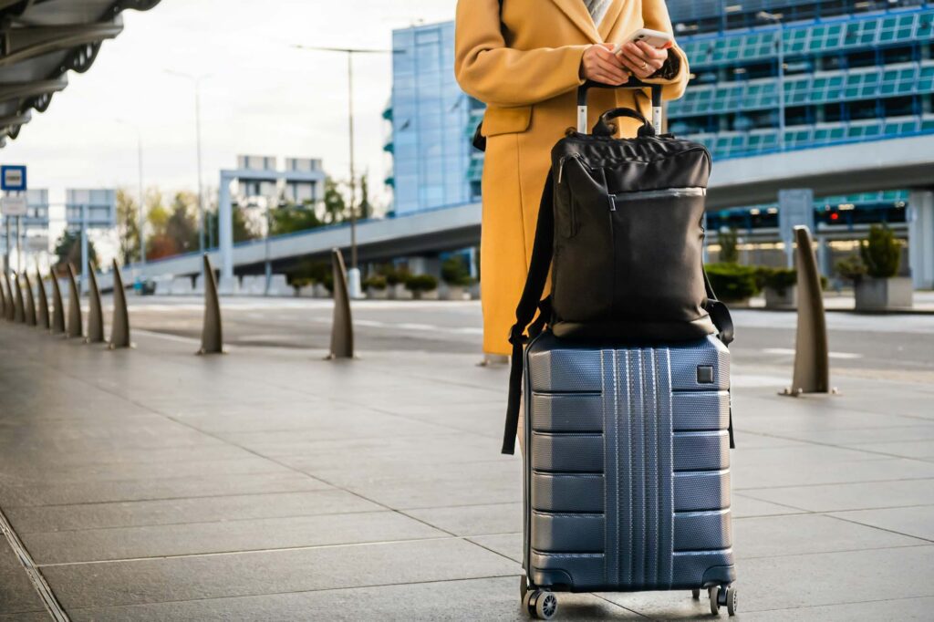 Woman traveler in coat with handbag and suitcase orders taxi